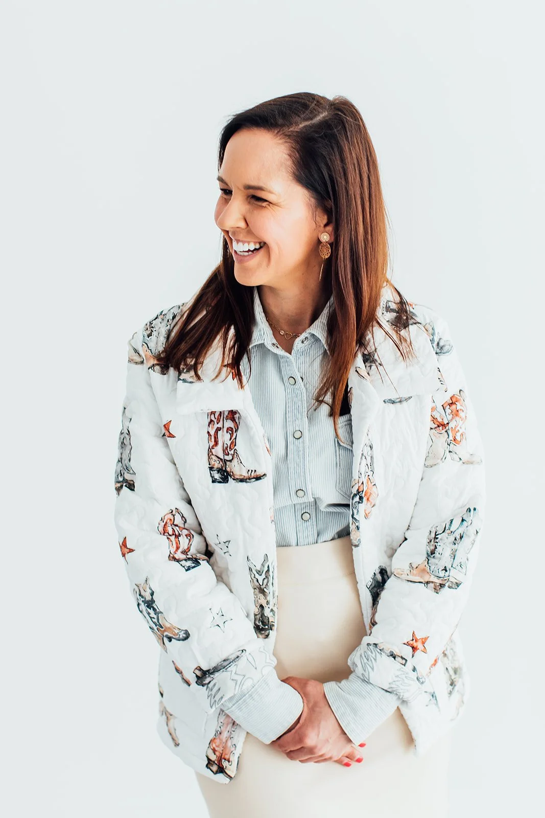 Katie Weiss, with brown hair, smiling and winking, wearing a white jacket with colorful patterns, a light blue striped shirt, and a beige skirt. She is the best StoryBrand Guide and Messaging Strategist in Fort Worth, Texas.