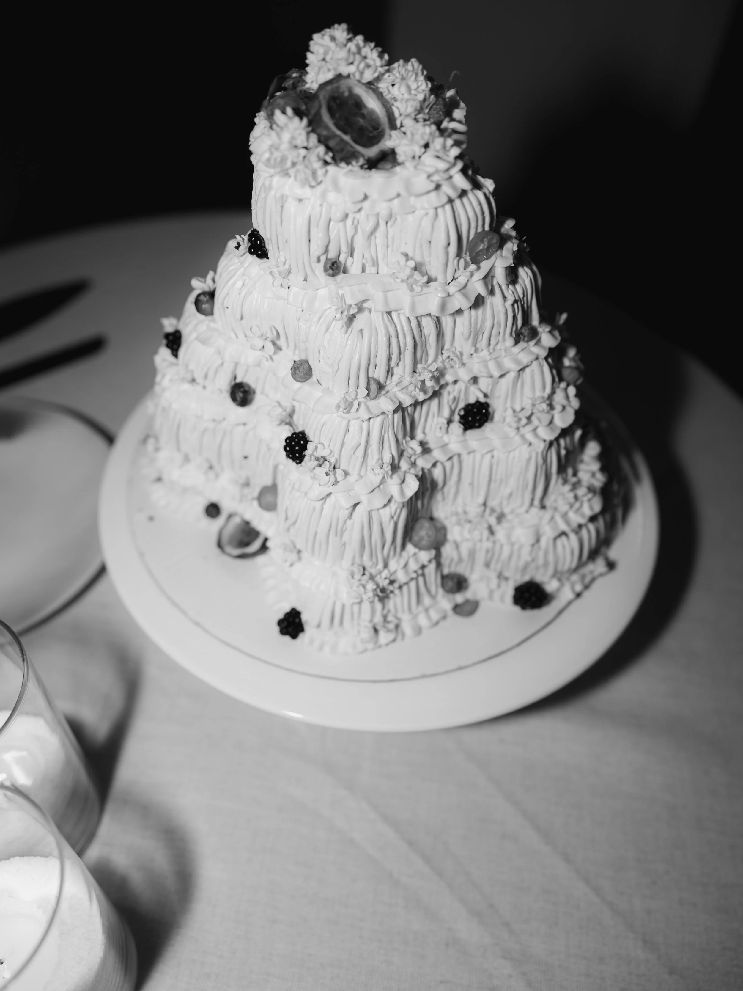 A tiered cake decorated with flowers and berries on a white plate.