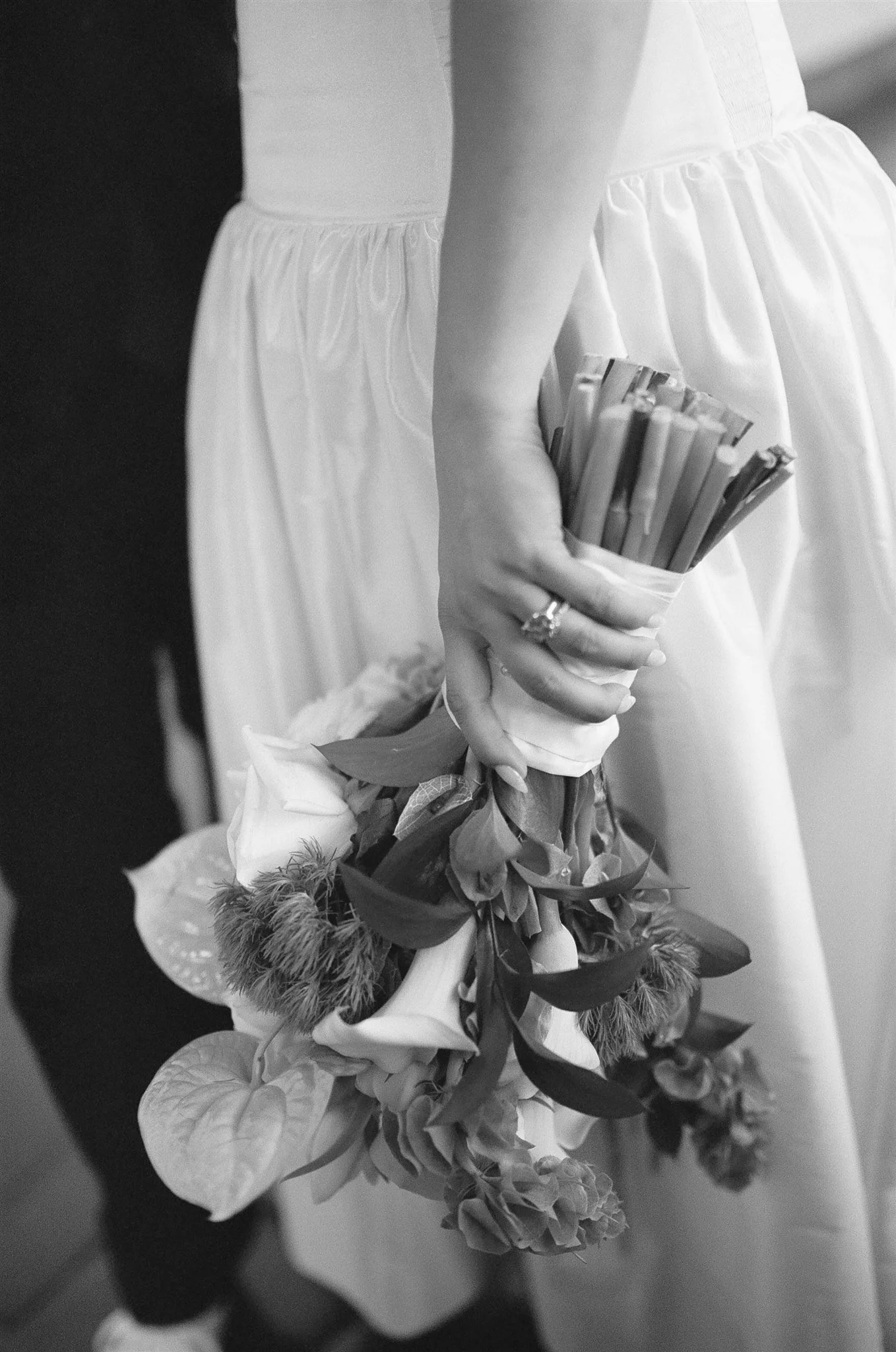 Close-up of a person holding a bouquet of flowers, with a dress and hand visible, in black and white.