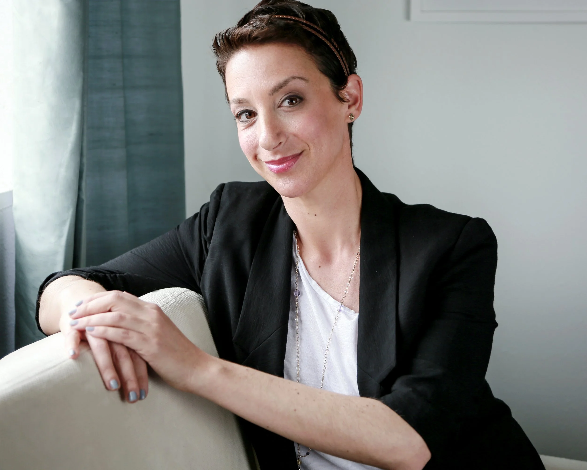 Close-up of a woman with a shaved head, wearing makeup, lying on a textured dark gray surface, and looking over her shoulder.
