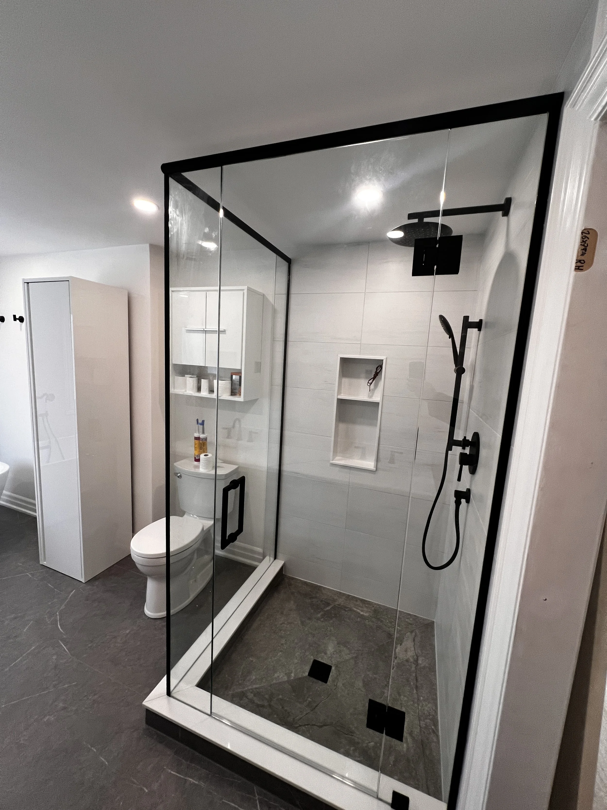 Modern bathroom with a fully enclosed glass shower, black fixtures, and a white toilet, with storage cabinets on the wall.