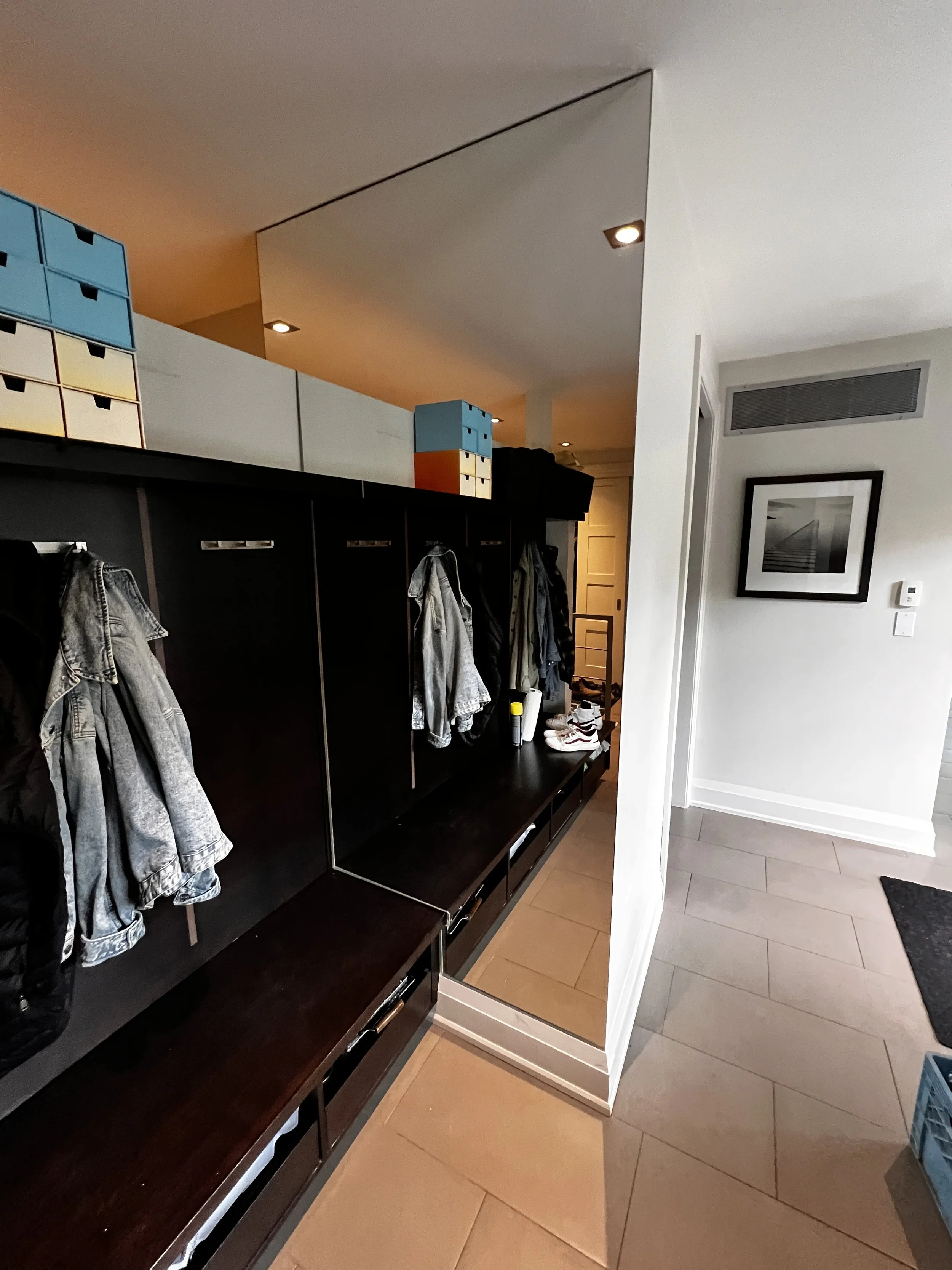 Entryway with black coat rack and cubby storage above, with jackets hanging from hooks, a mirror on the side, and a framed picture on the wall.