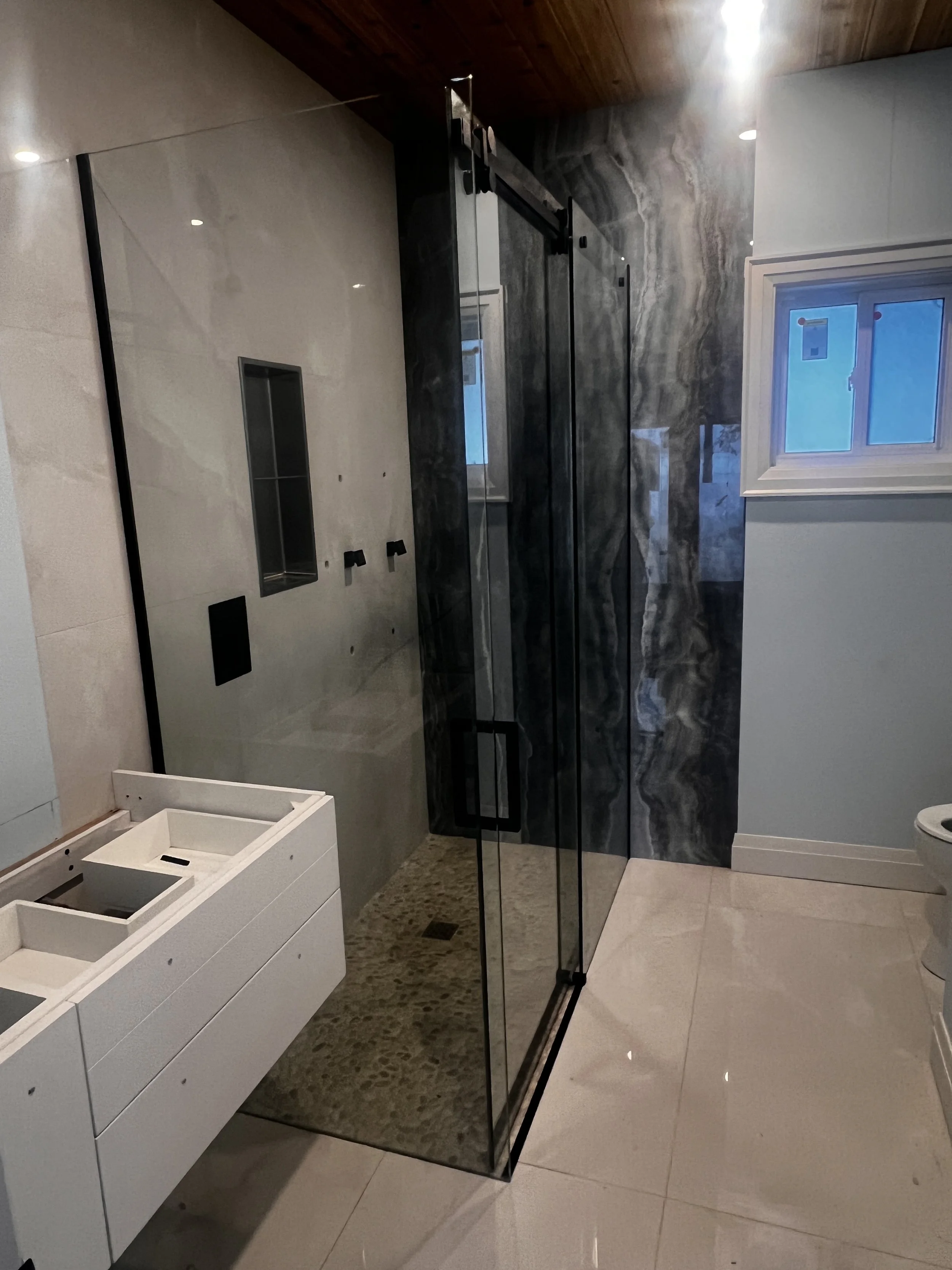 Modern bathroom with a glass shower, white vanity, and a small window.