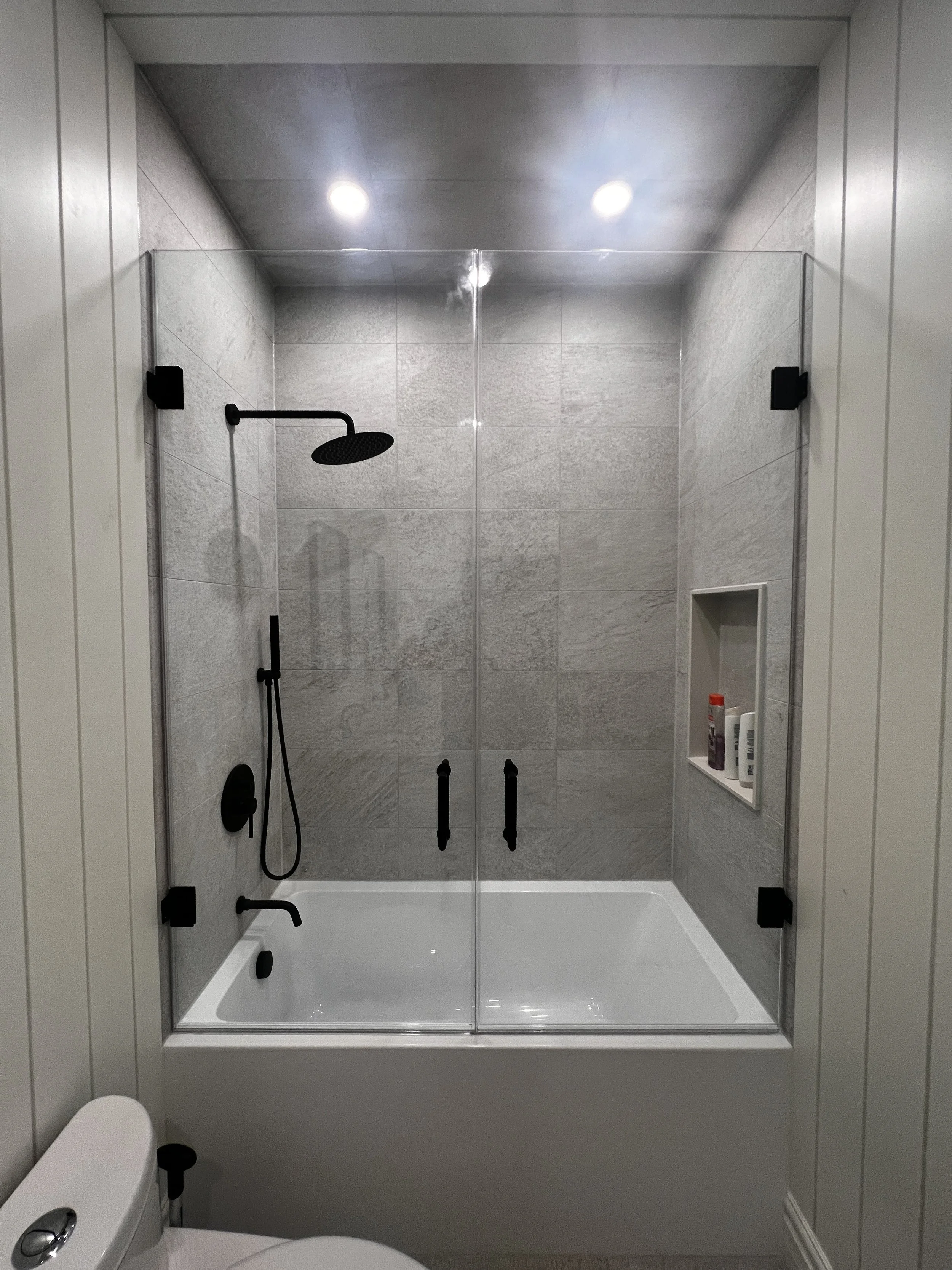 Modern bathroom with walk-in shower featuring gray tiled walls, black fixtures, and a clear glass enclosure.