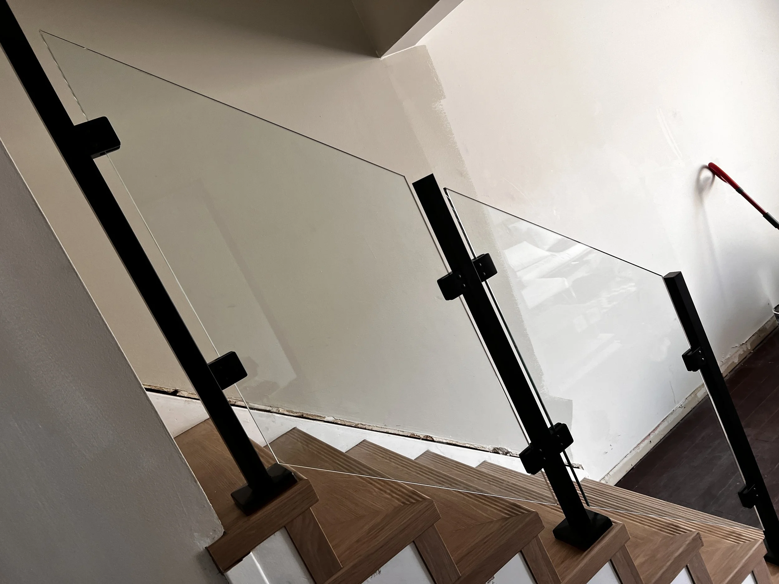Interior staircase with wooden steps, glass railing, and black metal supports in a residential setting.