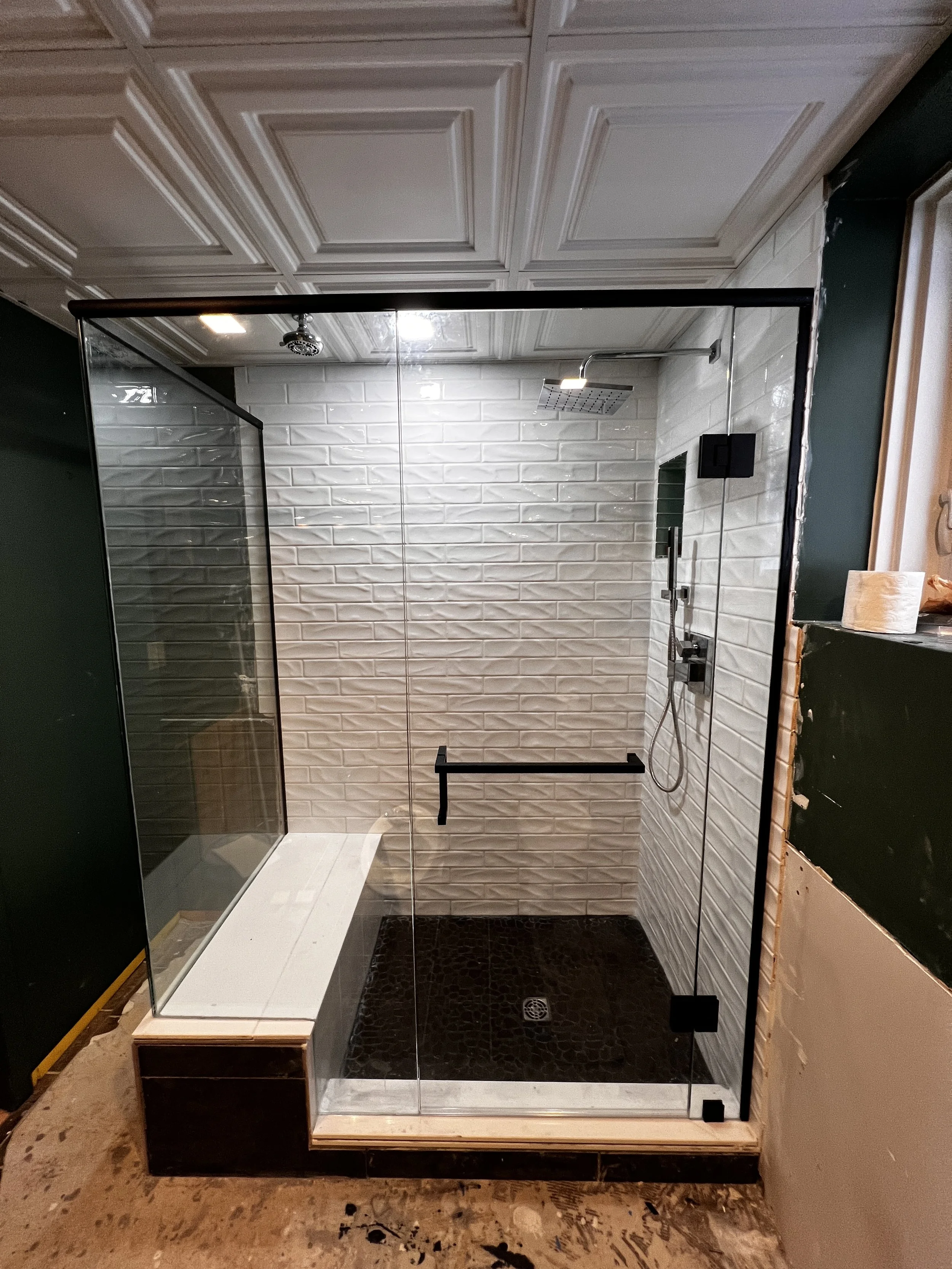 A modern walk-in shower with white brick tiles, a rain shower head, a handheld shower, and a glass enclosure.