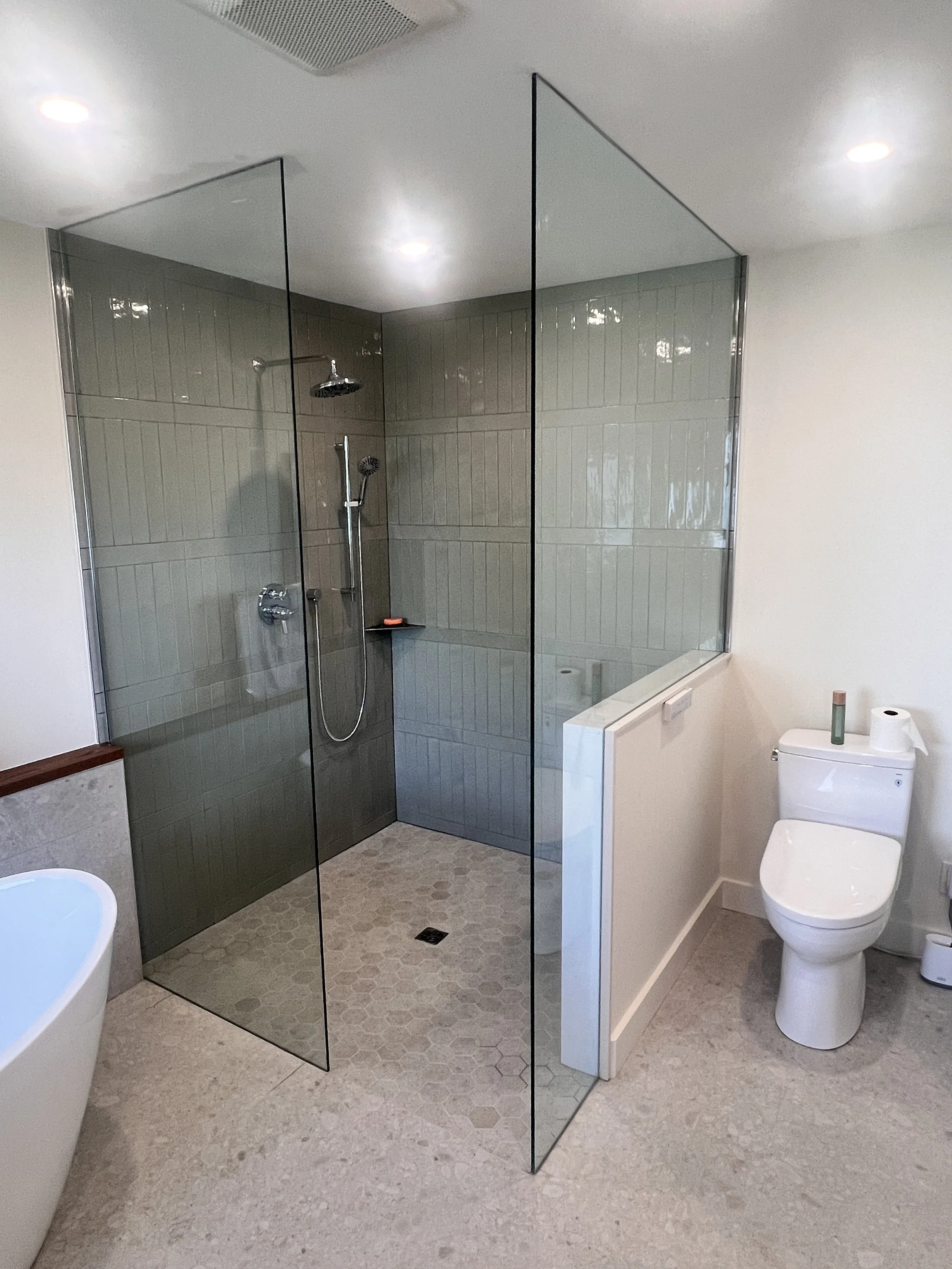 Modern bathroom with a walk-in shower with glass walls, a white toilet, a bathtub, and beige tile flooring.