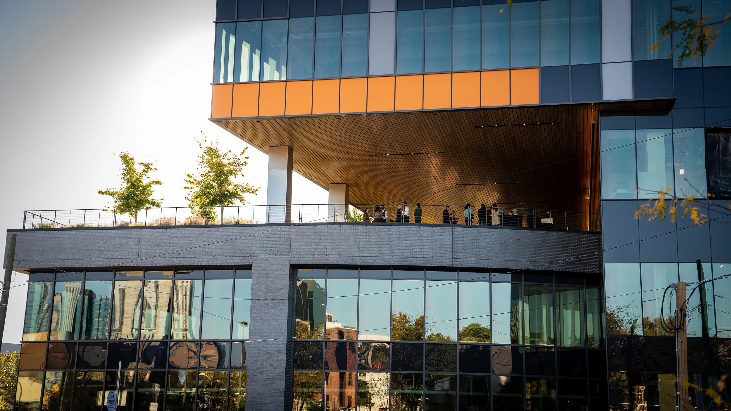 Exterior shot of the city reflected in the windows of University Place in Philadelphia with some people standing on their balcony.