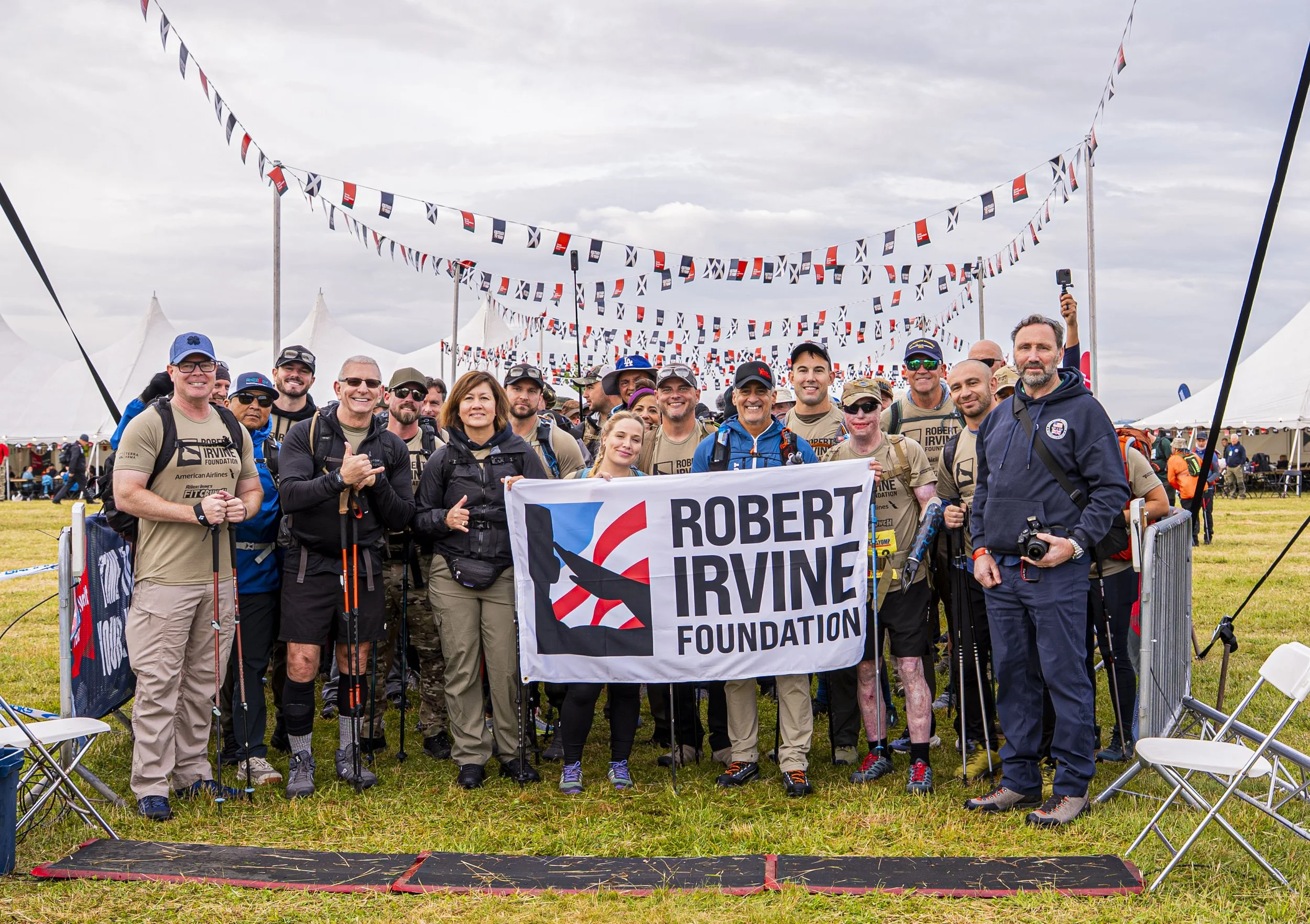 Robert Irvine stands with a group of veterans in a field of the Scottish Highlands with a sign with text: Robert Irvine Foundation.