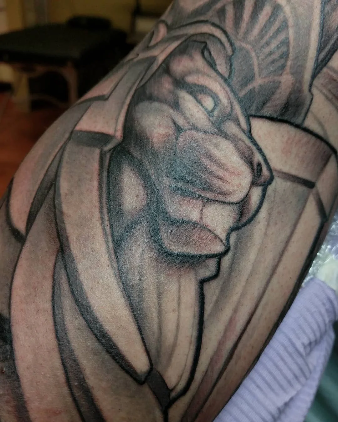 Close-up of a colored tattoo of a lion's face on a person's upper arm with a geometric background.
