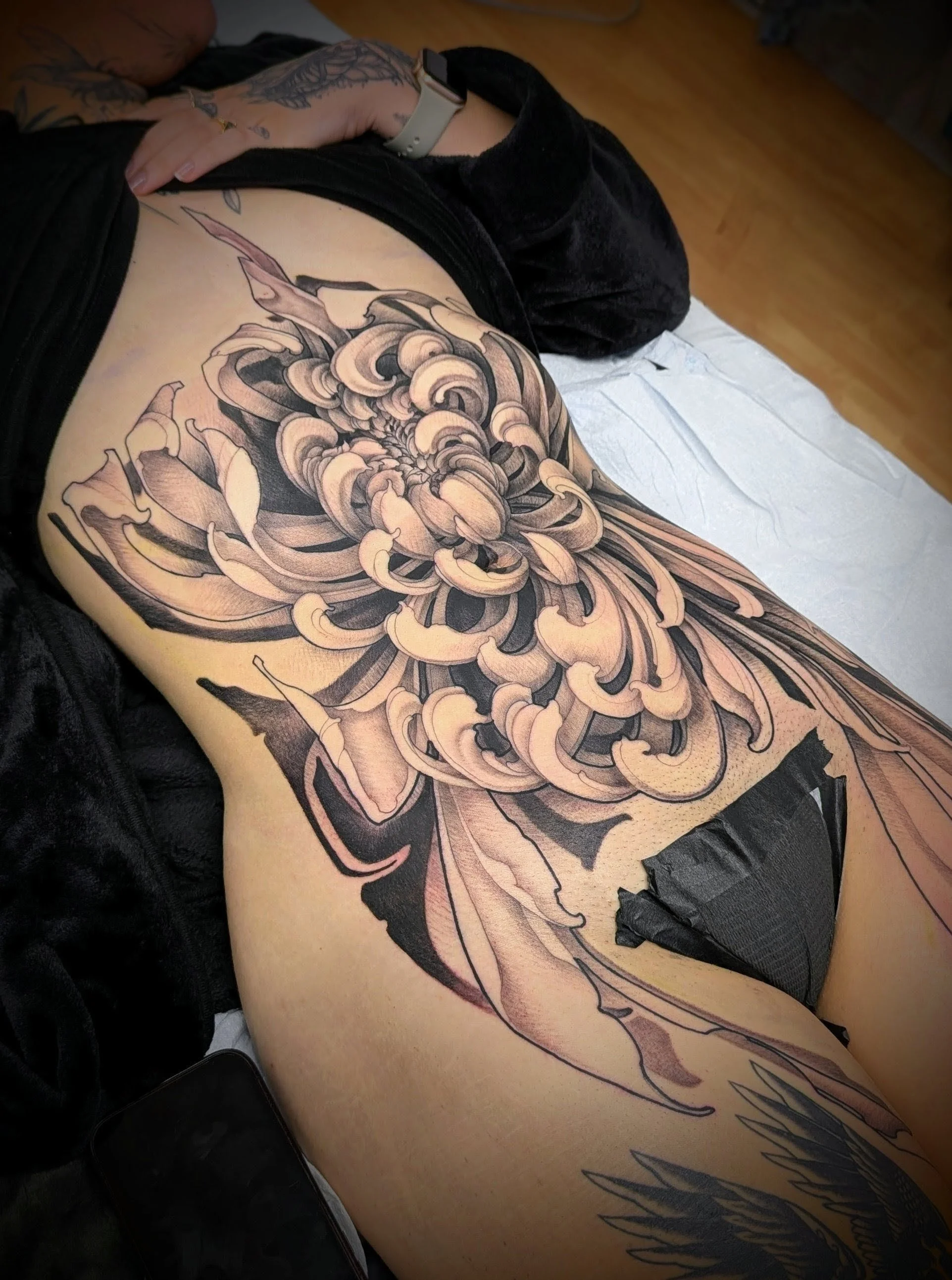 A person lying down with a large, detailed black and gray floral tattoo covering their side and thigh area.