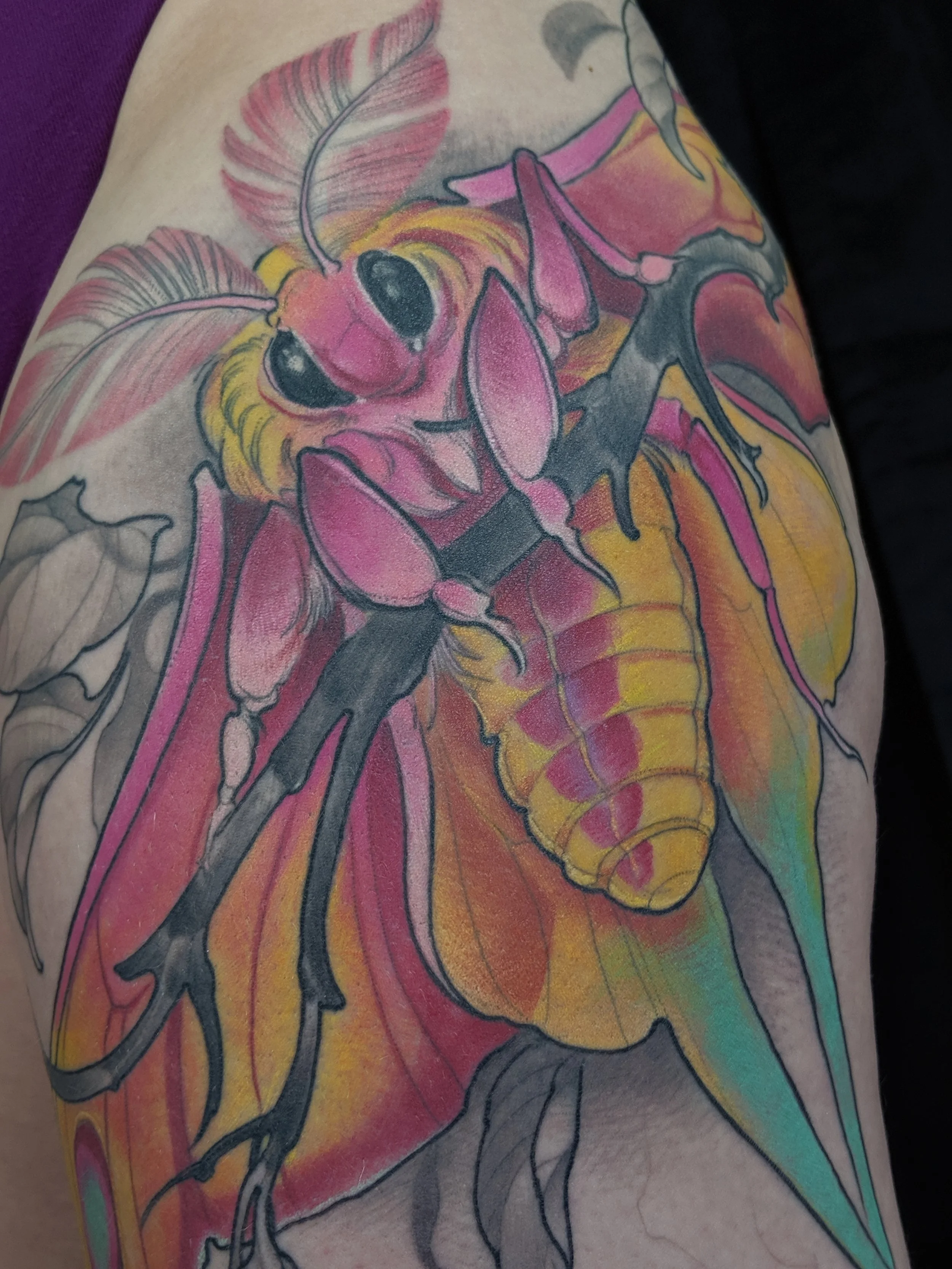 A colorful tattoo of an insect, possibly a bee or wasp, on a person's arm, with wings and detailed body in vibrant shades of pink, yellow, orange, and green.