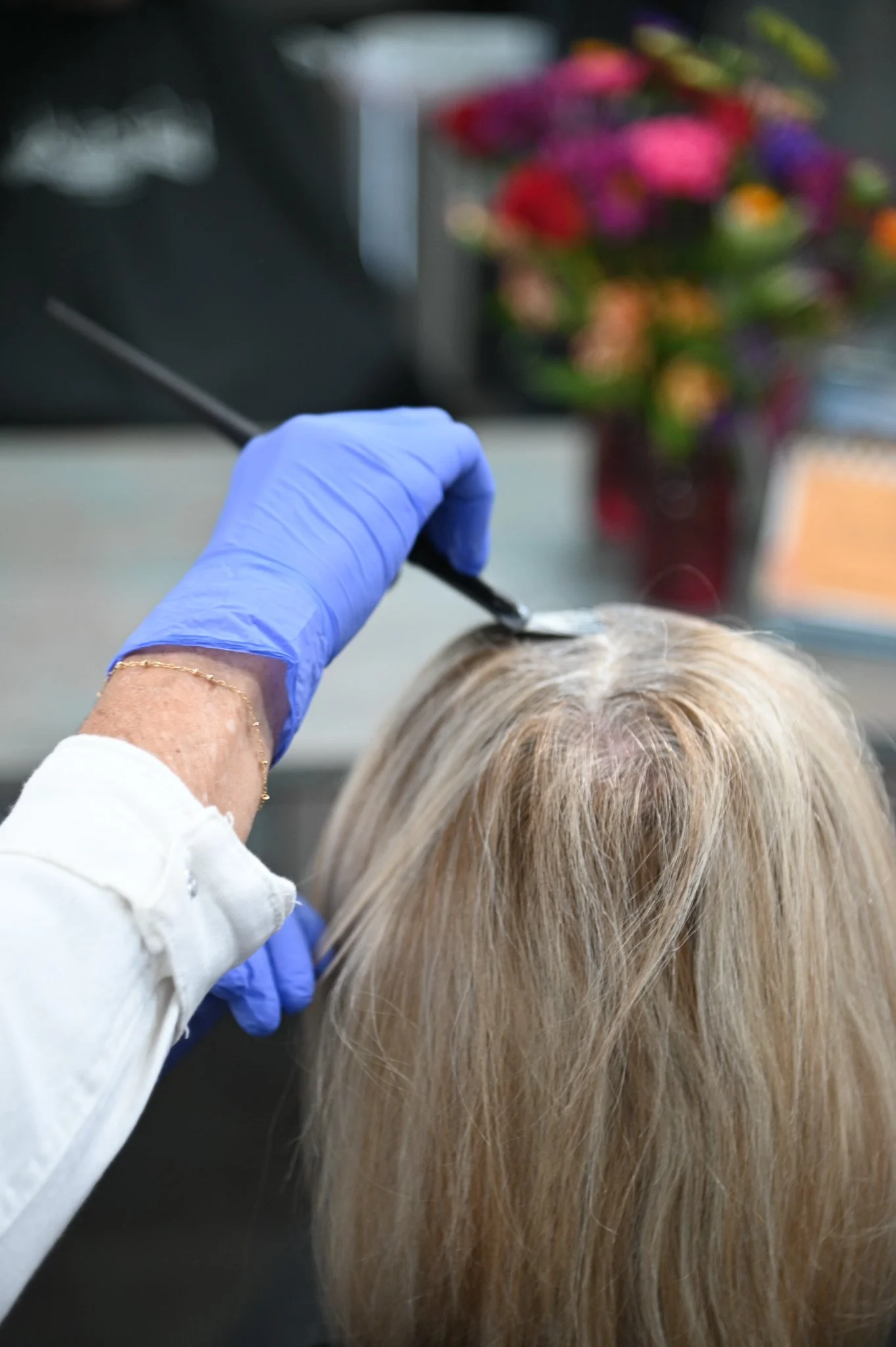 A woman getting her hair highlighted in a salon, with foil and clips in her hair, while a stylist applies product.