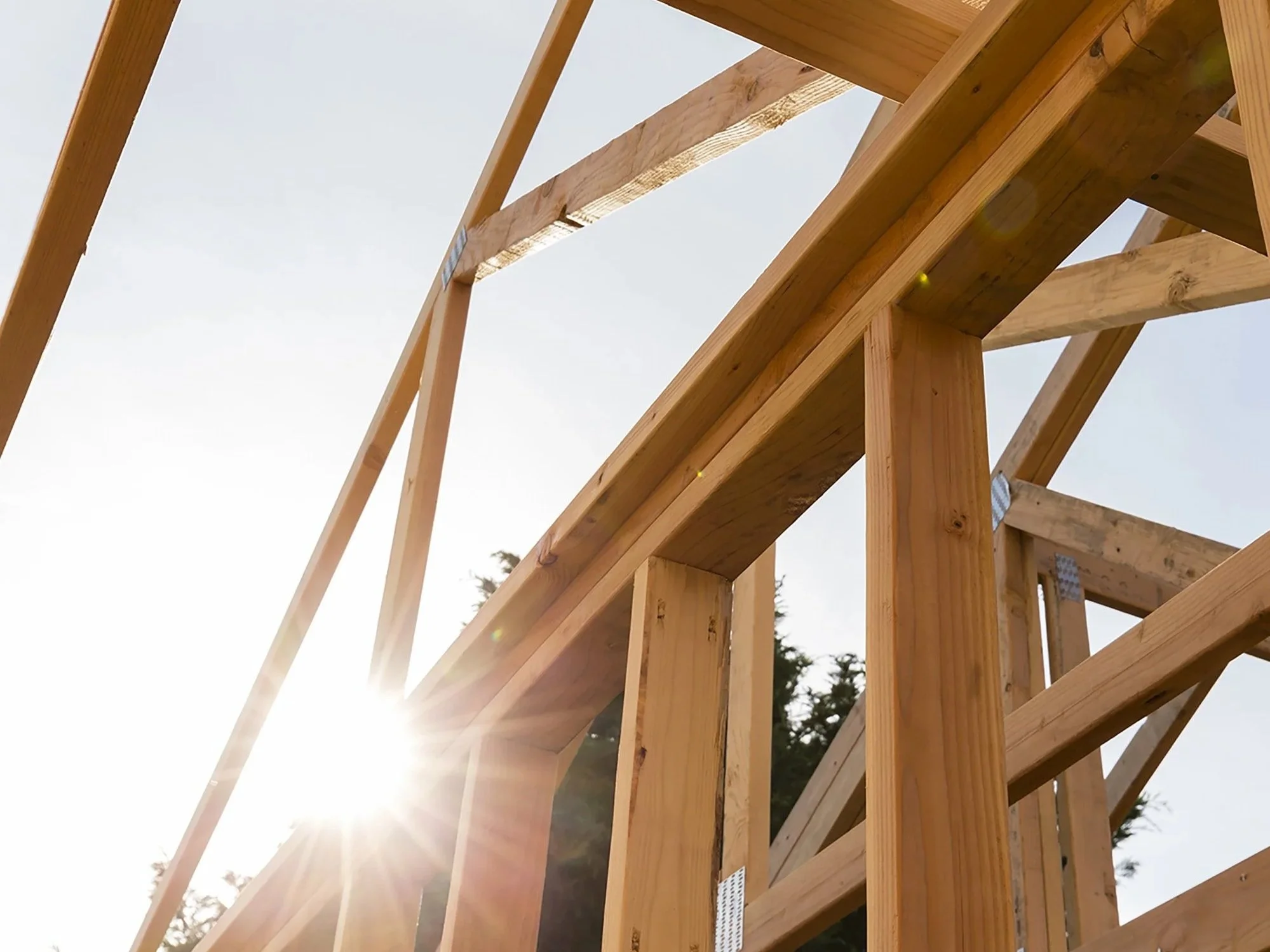 Wood framing and roof trusses of a new home under construction, with sunlight shining through