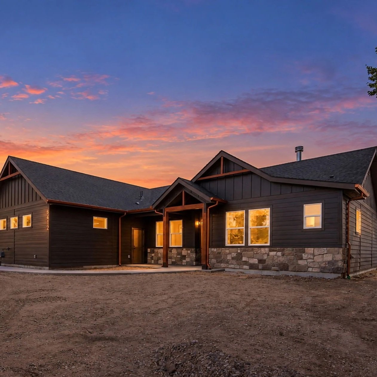 Bachman Custom Homes Trueman floor plan exterior with dark siding, stone accents, and timber porch at sunset.