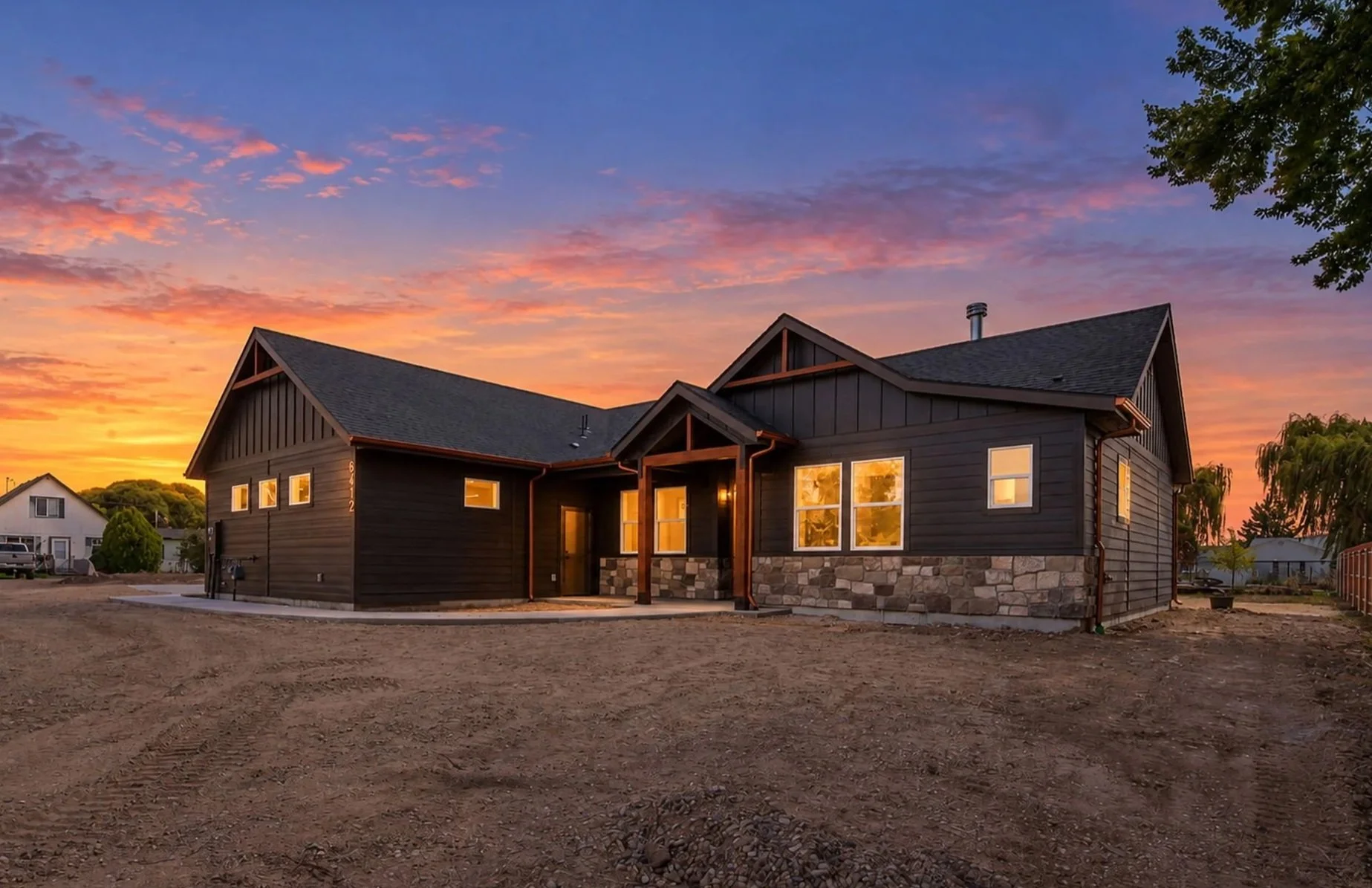 Exterior of the Trueman floor plan by Bachman Custom Homes at sunset, with dark siding, stone accents and a timber-framed entry.