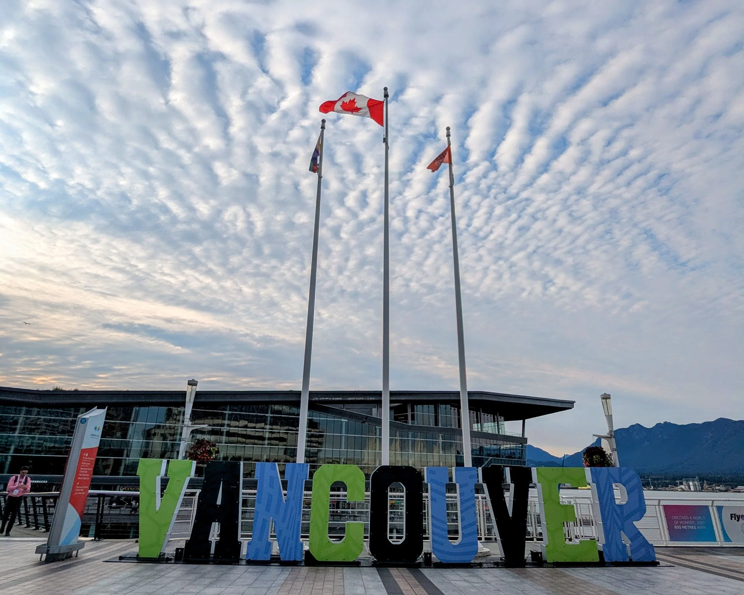 Large, colorful Vancouver sign and Canadian flags at Canada Place