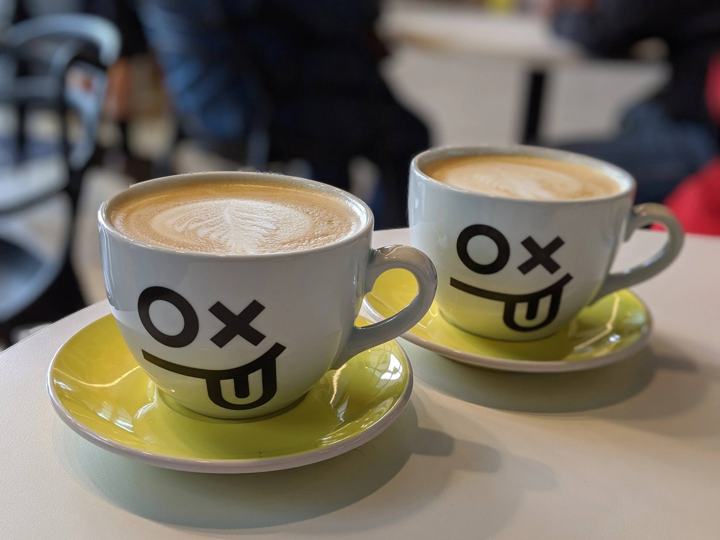 Two coffee cups with faces - an o and an x for eyes, and the tongue sticking out, sitting on yellow saucers
