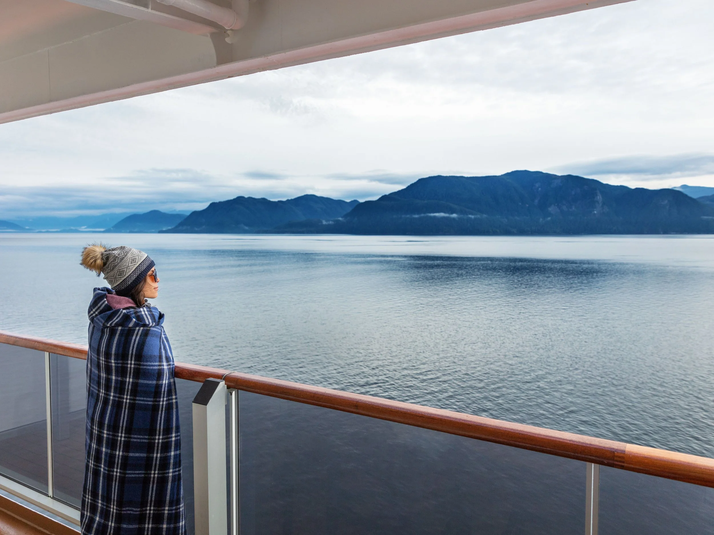 Traveler gazing out at dramatic Alaska glacier landscape from cruise ship deck