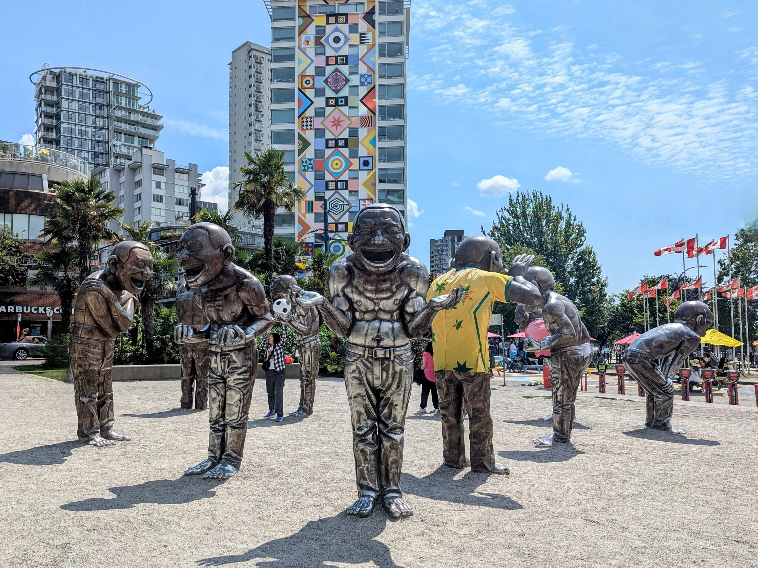 Sculptures of oversized bronze figures, laughing uproariously, along a beach front, some dressed in soccer jerseys for the World Cup.