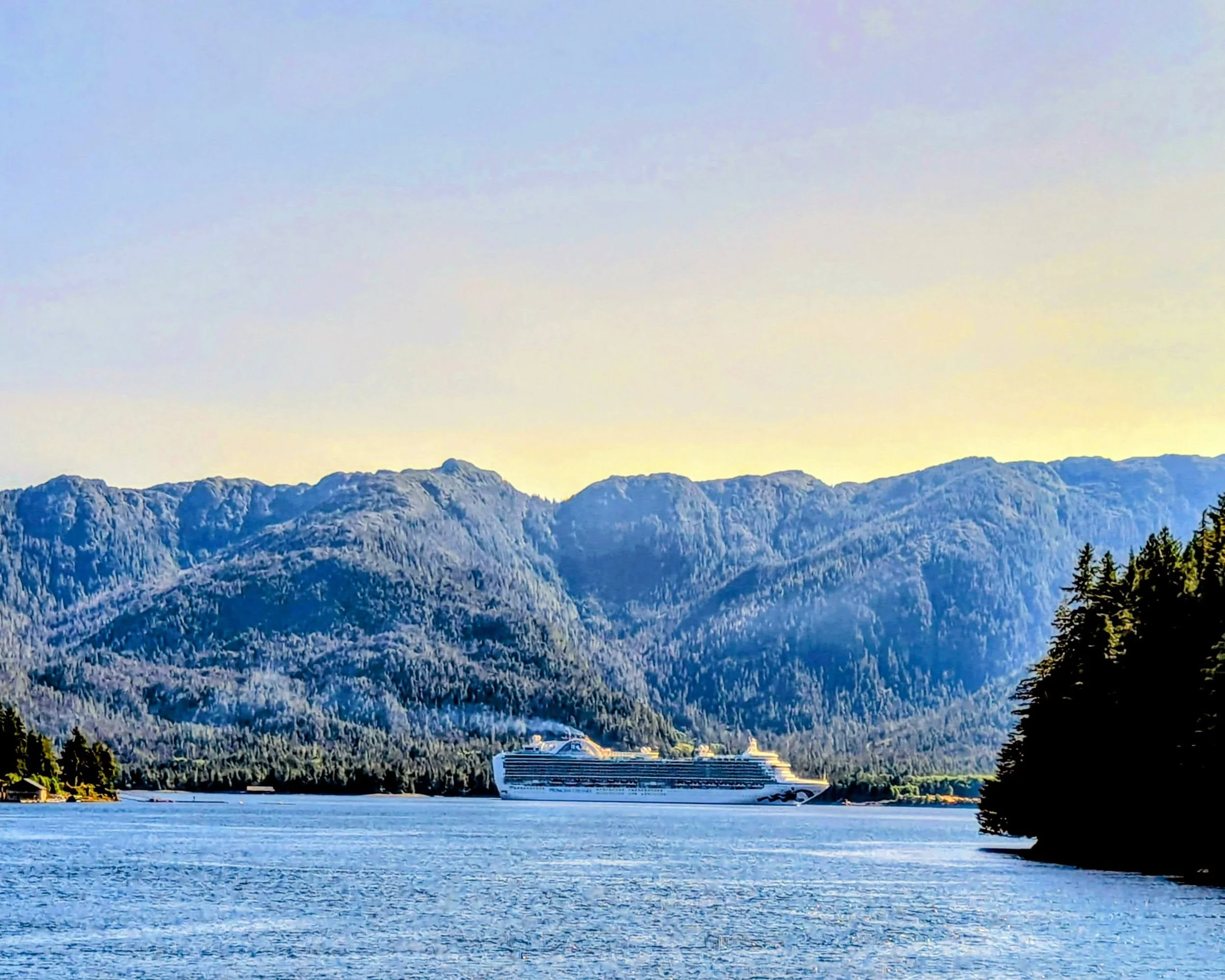 Large cruise ship sailing Alaska's Inside Passage at twilight, mountains and sea visible