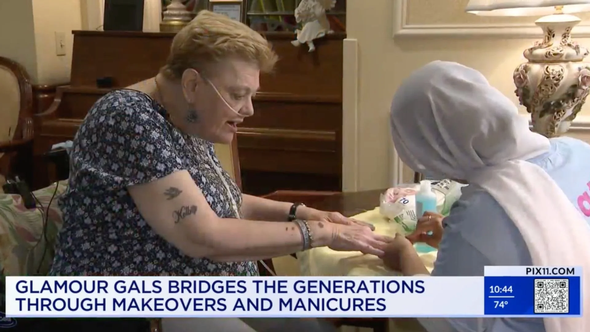 A woman receiving a manicure from a manicurist in a well-lit room, with a decorative lamp and framed picture on the wall in the background.