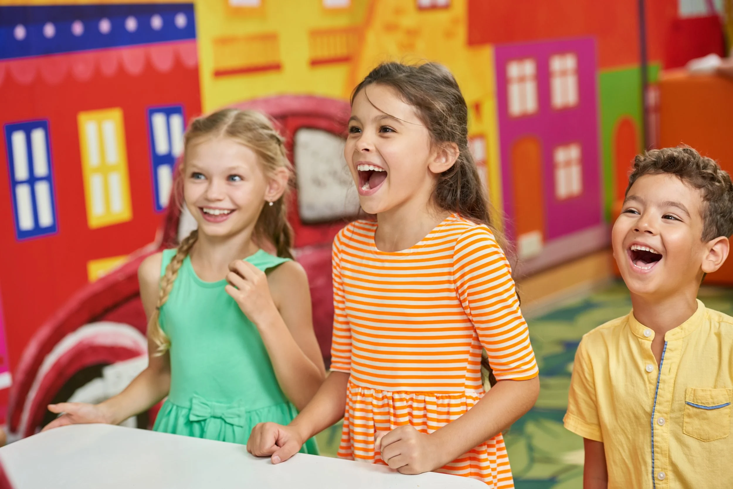 Three children laughing and having fun in a colorful indoor play area.
