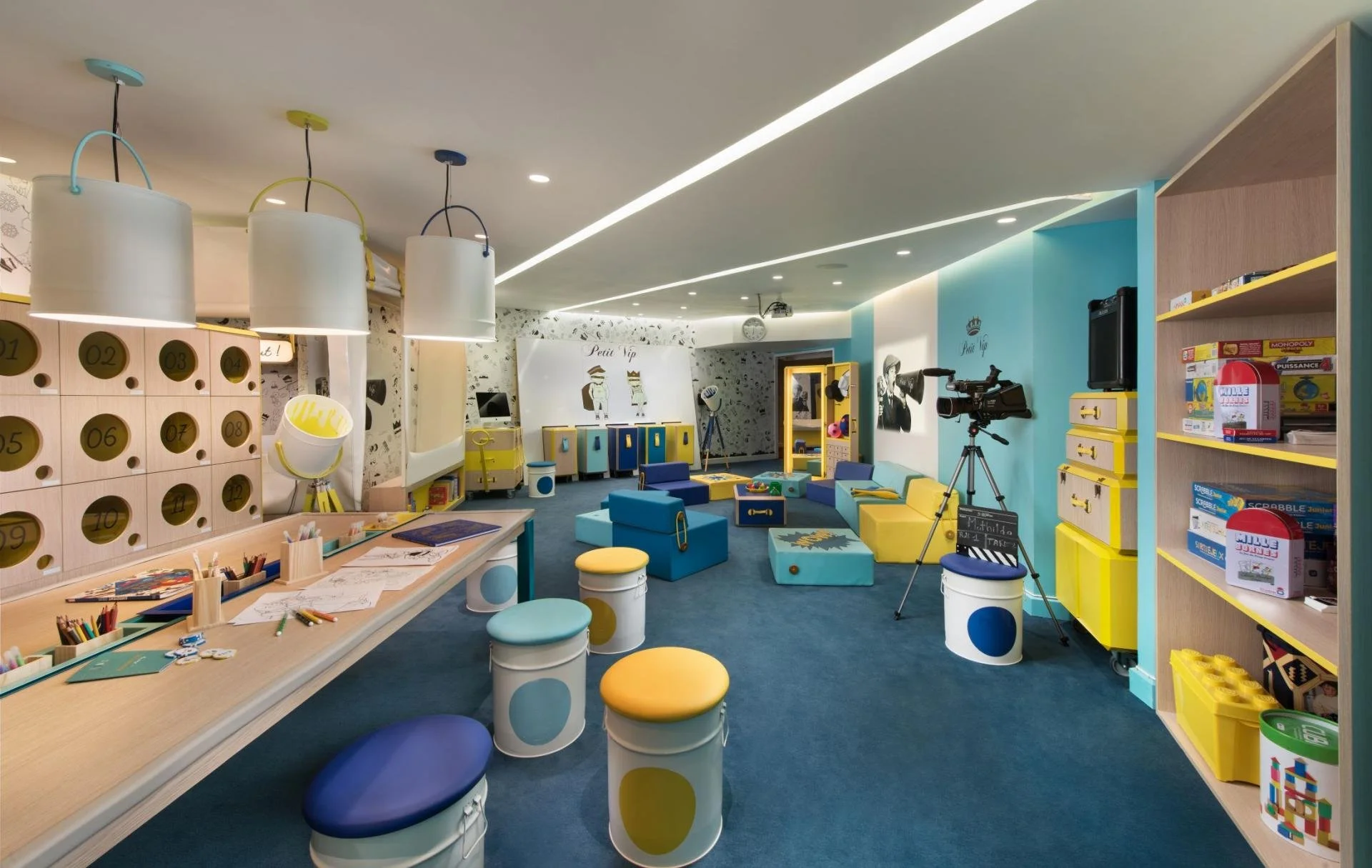 Colorful children's play and activity room with various toys, furniture, and decorations, including lockers, sofas, and a camera setup.