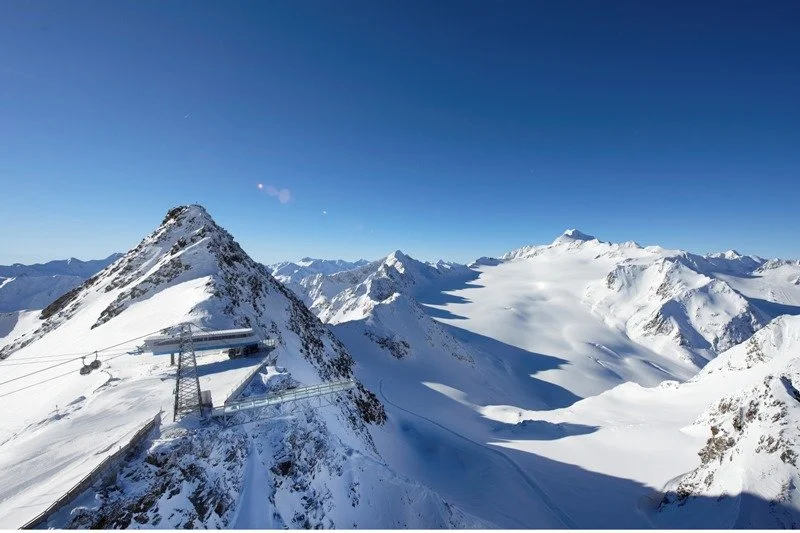 Snow-covered Solden mountain range with a ski lift station on a peak and clear blue sky