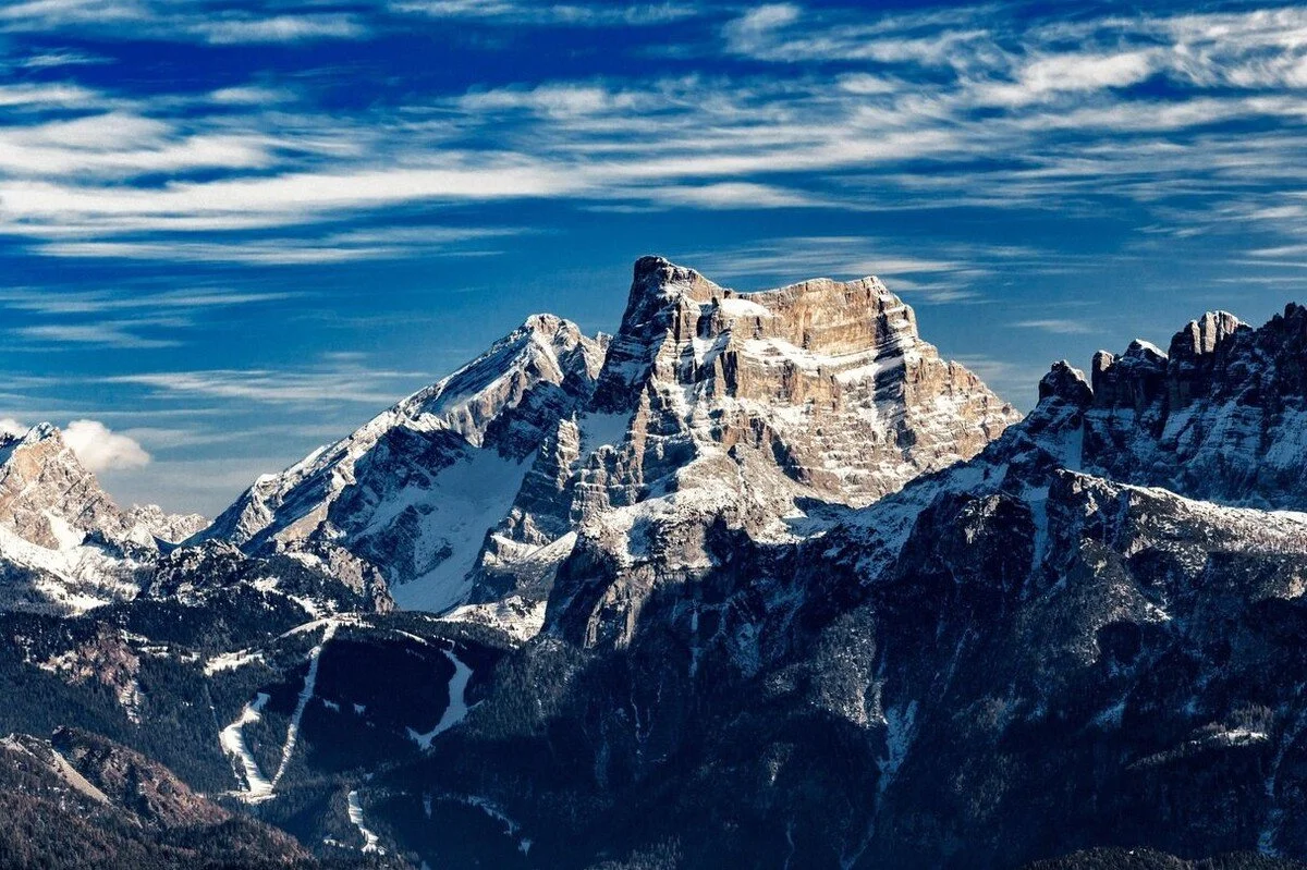 Snow-capped mountain peaks under a blue sky with wispy clouds.