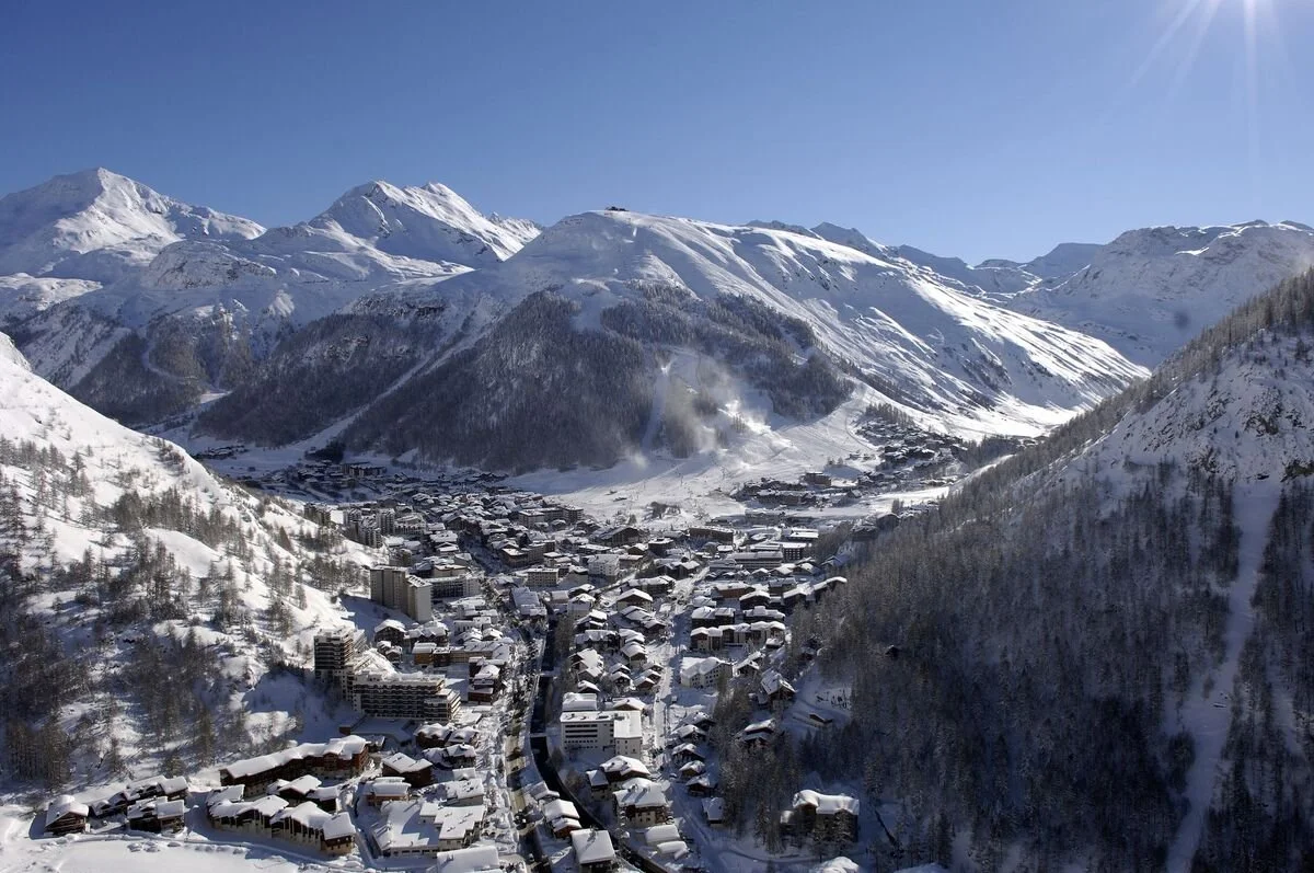 Snow-covered Val d'Isere mountain village surrounded by tall, snowy peaks on a clear, sunny day.