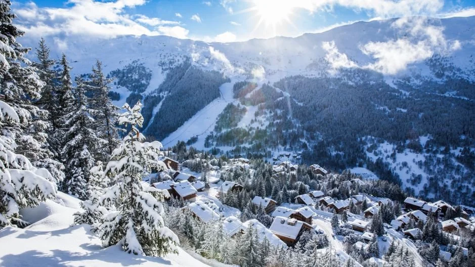 Snow-covered Meribel mountains, pine trees, and a small village with houses in a winter landscape