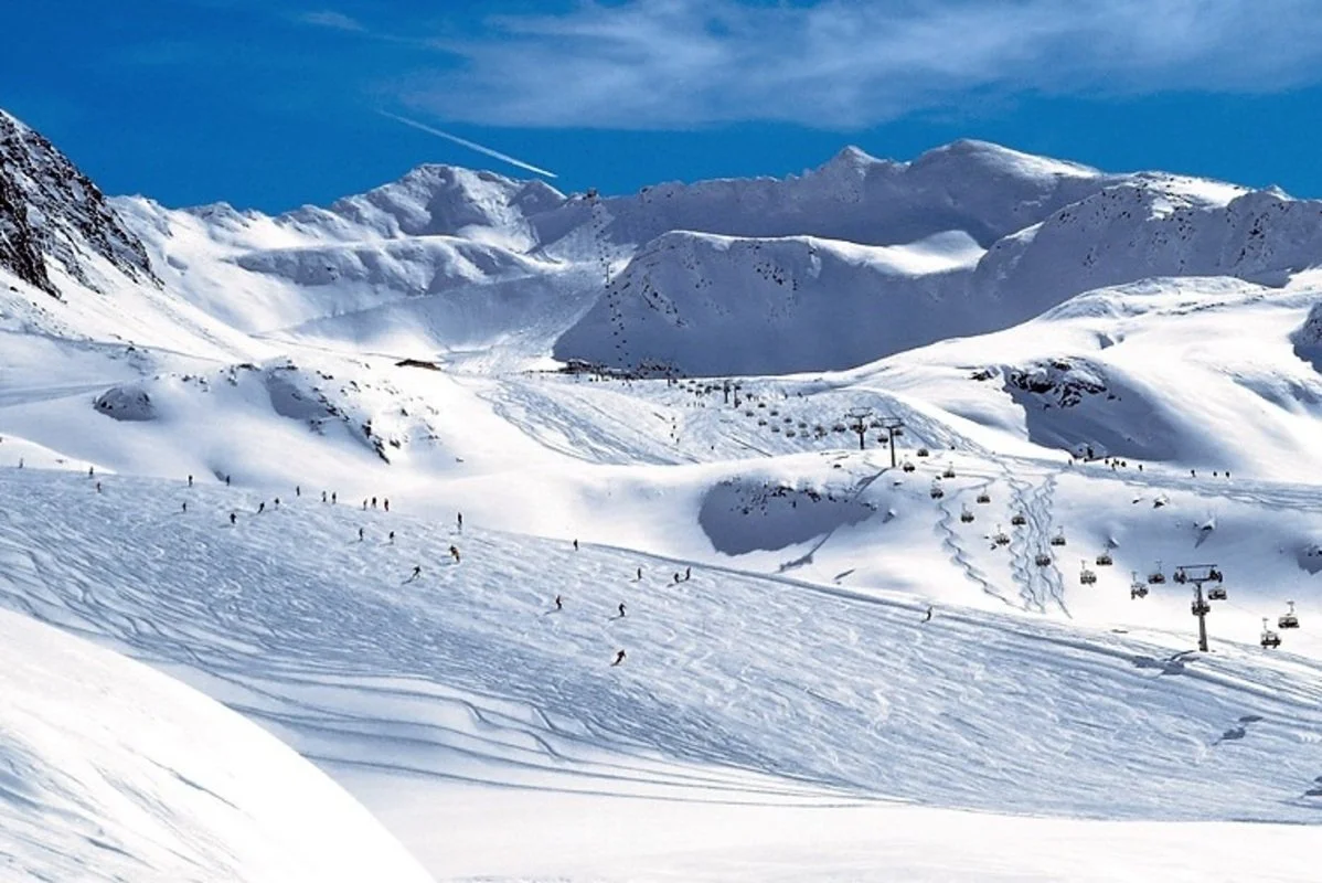 A snowy mountain landscape in Solden with skiers on the slopes, ski lifts, and a clear blue sky.