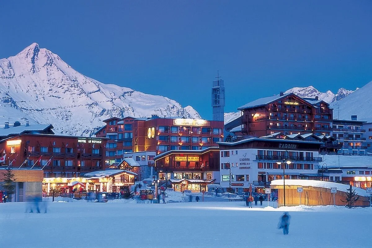 Snow-covered Tignes mountain town at dusk with illuminated buildings and a mountain backdrop.
