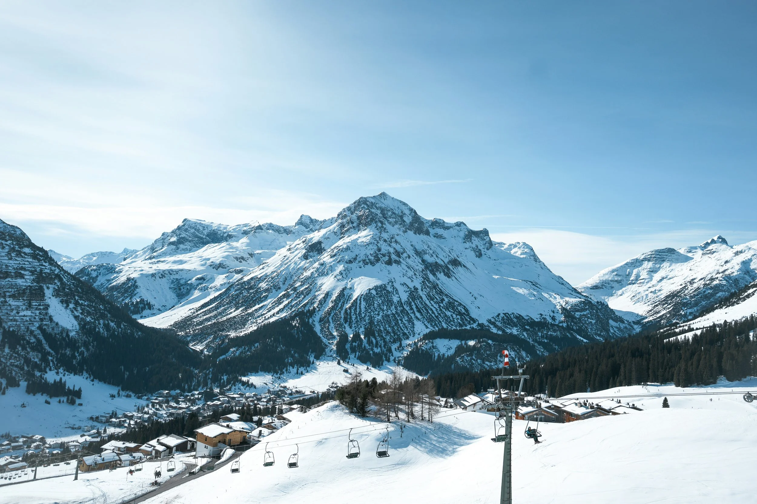 Snow-covered mountains overlooking Lech ski resort village with chairlifts and ski runs, under a clear blue sky.