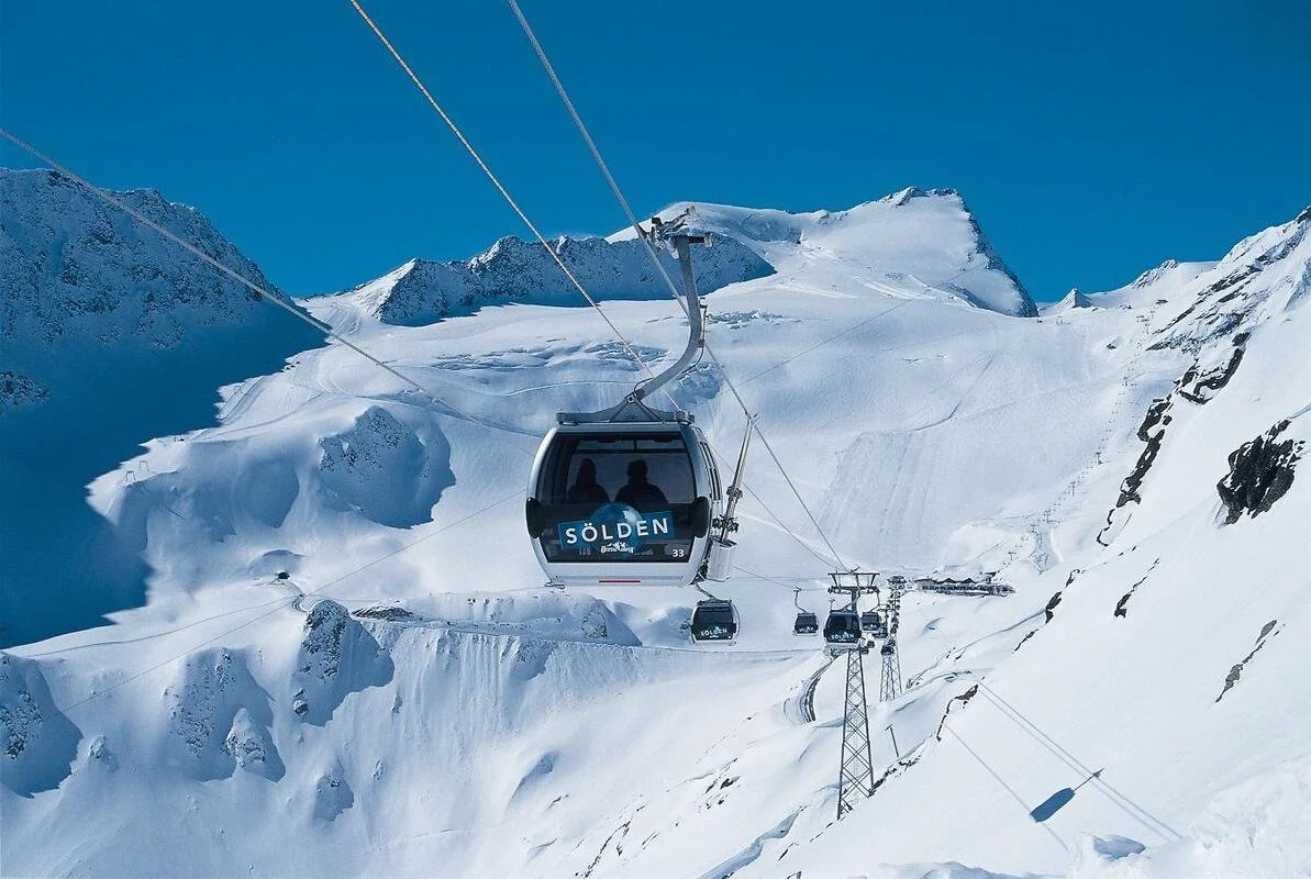 A gondola lift in Solden traveling over a snow-covered mountainous landscape with clear blue sky in the background.