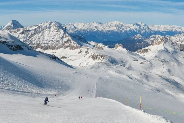 Snow-covered mountains with skiers on a trail and ski poles, clear blue sky above.