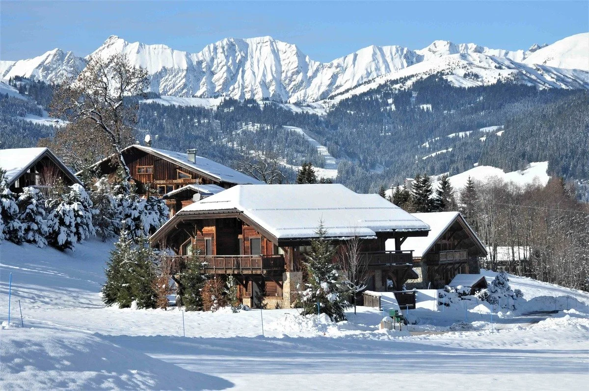 Snow-covered Megeve mountain landscape with rustic wooden cabins surrounded by snow and pine trees.