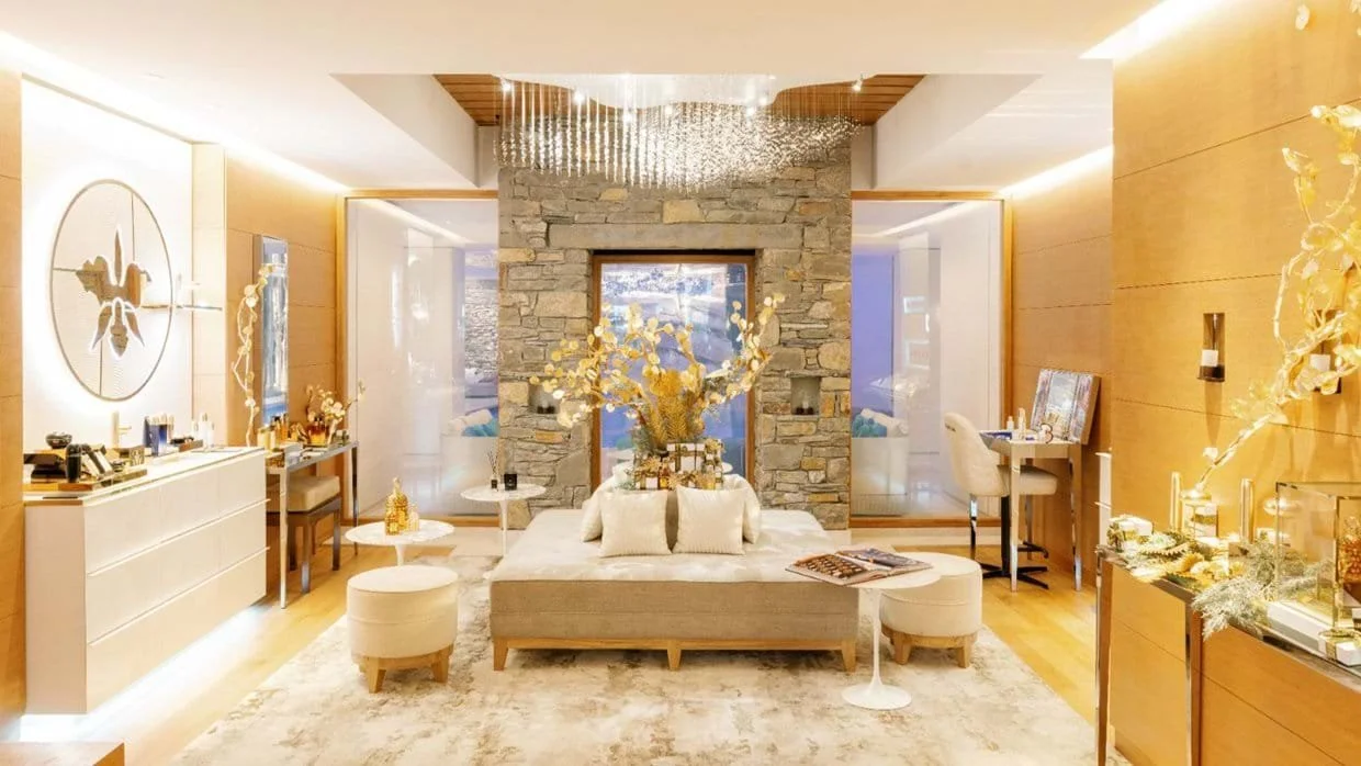 Elegant living room with a stone fireplace, beige sofa, matching ottomans, and decorative gold accents, illuminated by warm lighting and modern decor.