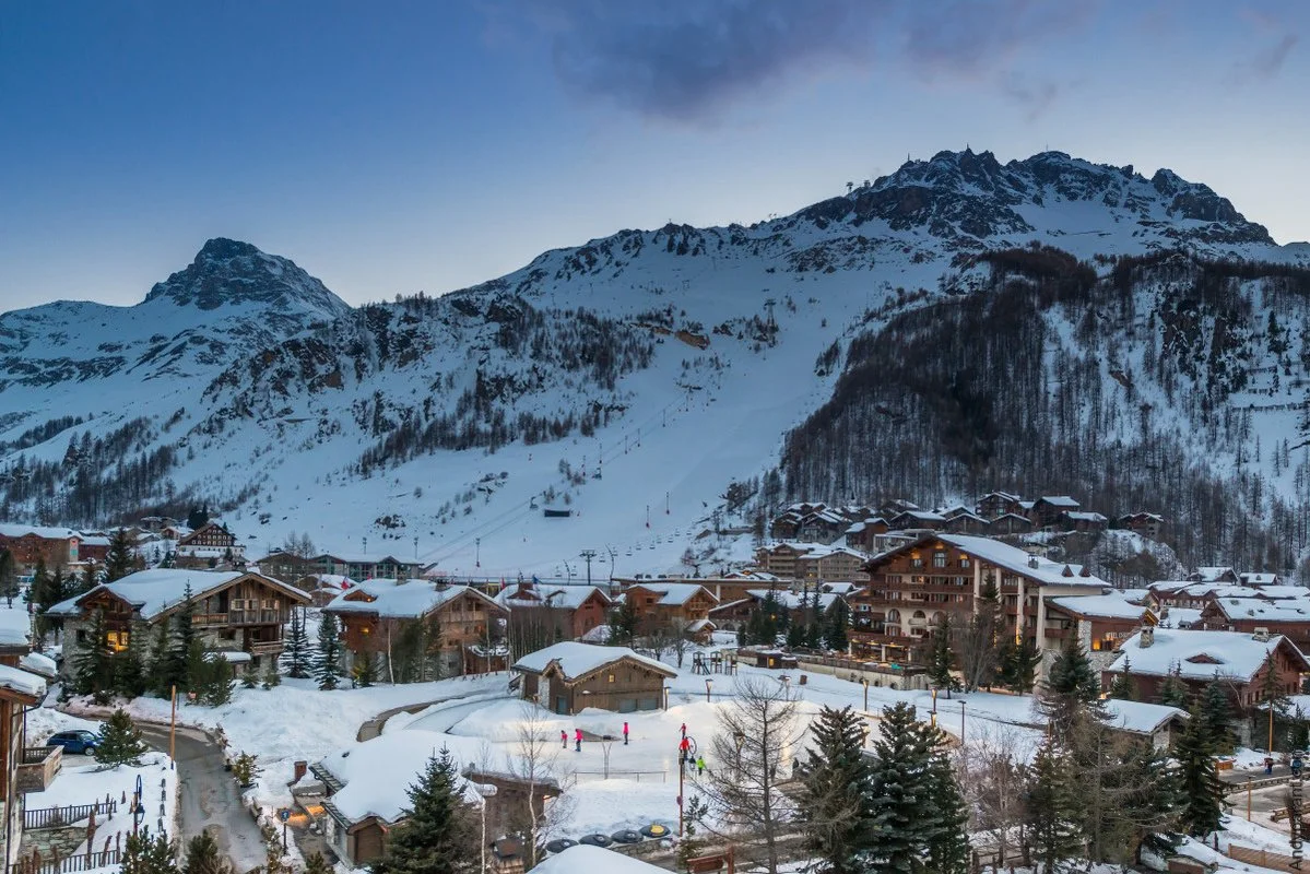 Snow-covered Val d'Isere mountain village with skiers and ski lifts, surrounded by tall mountains.