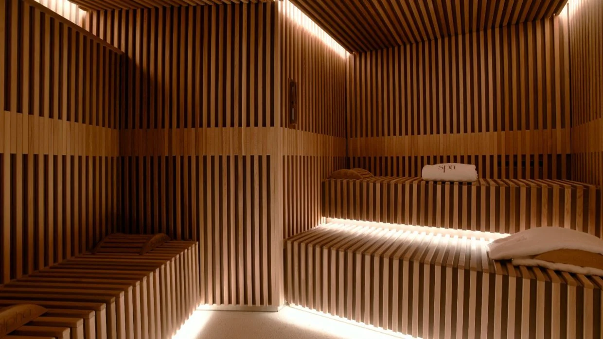 Interior of a modern sauna with wooden slat walls, benches, and ambient lighting.