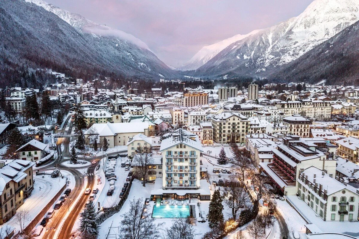 Snow-covered Chamonix town nestled in a mountainous landscape with buildings, roads, and a swimming pool in the foreground.
