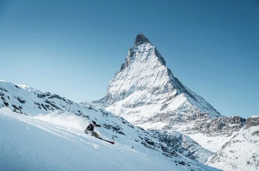 A skier descending a snowy slope in Zermatt with the Matterhorn mountain in the background under a clear blue sky.