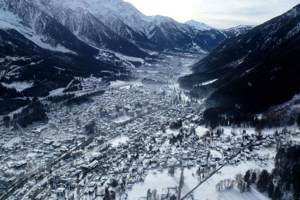 Aerial view of a snowy Chamonix surrounded by mountains and forest during winter.