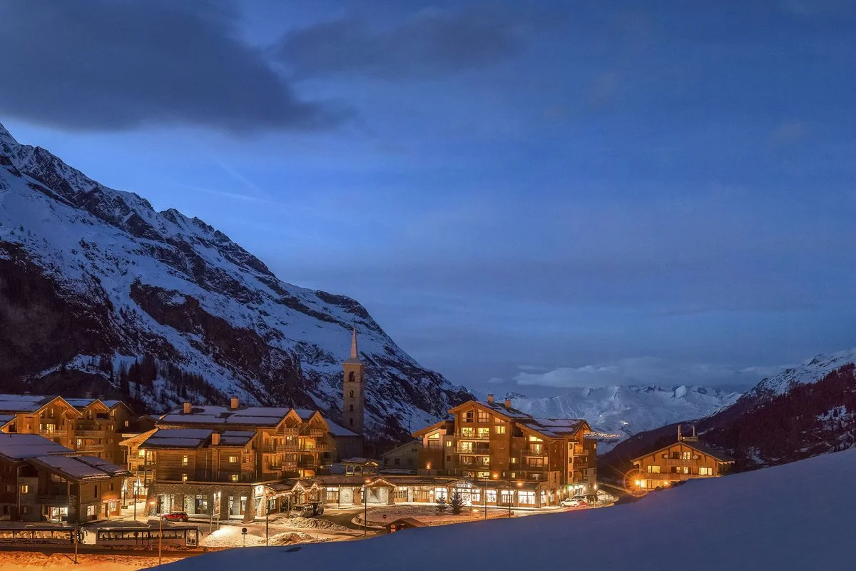 Snow-covered Tignes mountain village at dusk with illuminated buildings and a church steeple.