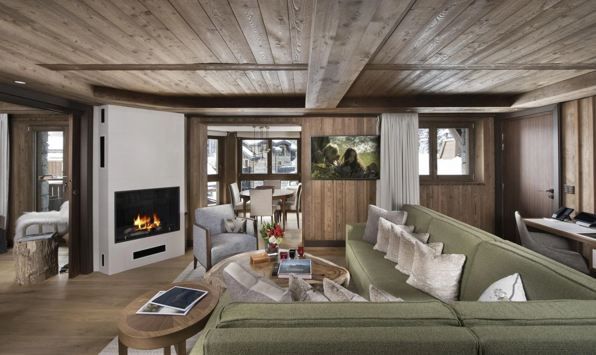 Living room with wood paneling, fireplace, green sofa, armchair, coffee table, dining area, and wall-mounted TV