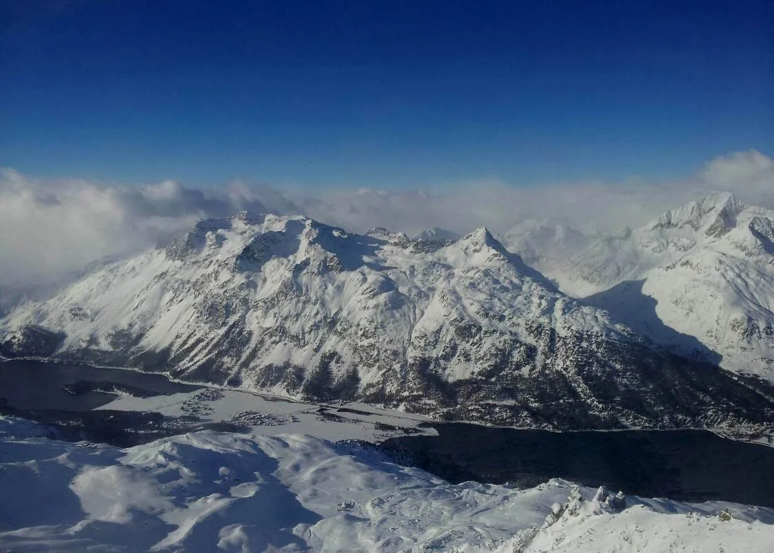 Snow-covered St Moritz mountains under a blue sky with some clouds.
