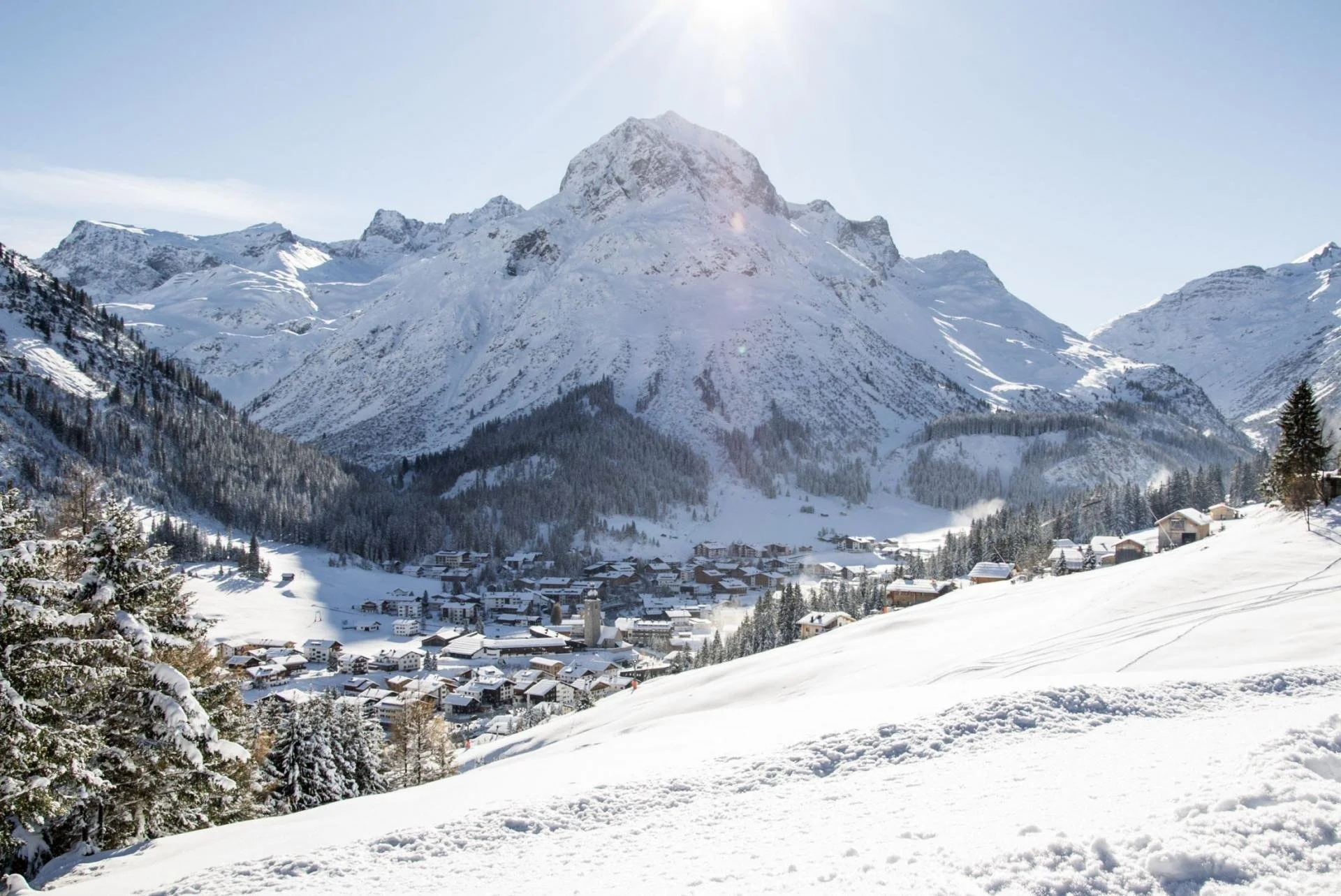 Snow-covered Lech mountain village with a large mountain in the background and a clear blue sky.