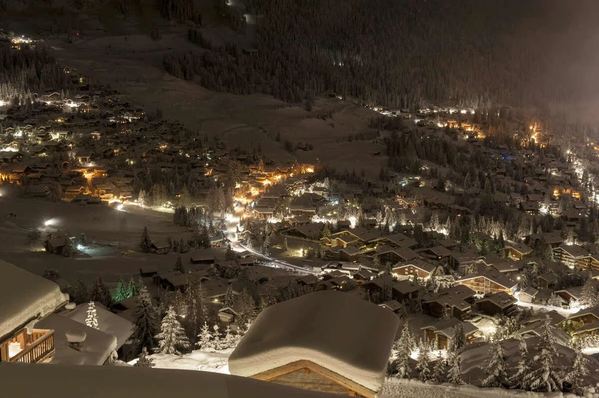 Nighttime view of a snow-covered Verbier mountain village with illuminated houses and trees.