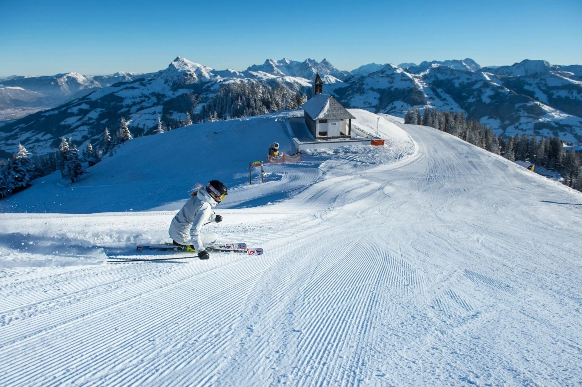 A person skiing down a snowy slope in Kitzbuhel with snow-covered peaks in the background.